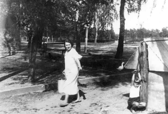 Rok i miejsce wykonania: 1940 r., Puszcza Mariańska, gm. Puszcza Mariańska, pow. żyrardowski, woj. mazowieckie.

Fotografia przedstawia kobietę niosącą wiadro z wodą oraz dziecko bawiące się przy studni. W tle widać rozległy, zadrzewiony teren z ławką oraz chodzącą gęś, a w oddali kury.

Na odwrocie zdjęcia napis: „››Zaopatrzenie‹‹ w wodę. Zdjęcie wykonane w 1940 r. /Wodę ze studni gminnej dźwiga żona sekretarz gminy/. Wykonane przez foto-amatora W. Szpruta we wsi Puszcza Mariańska, b, gm. Korabiewice, pow. skierniewickim” (pisownia oryginalna).

Autor zdjęcia: W. Szprut.

Zdjęcie ze zbiorów prywatnych, nadesłał: Władysław Szczęśniak z Łodzi.

Nr kat. 20-6