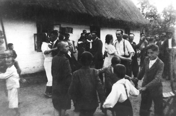 Rok i miejsce wykonania: ok.1930-35 r., Chorośnica, Podole, obecnie Ukraina.

Fotografia przedstawia ludzi tańczących na podwórzu przed chłopskim, bielonym domem krytym strzechą. Dorośli są odświętnie ubrani i tańczą w parach. Wśród nich widać też tańczącą grupkę czterech lub pięciu chłopców. W tle widoczni są mężczyźni przyglądający się zabawie.

Autor zdjęcia: Wanda Lebiedzińska.

Zdjęcie ze zbiorów prywatnych, nadesłała: Aleksandra Gancarz z Andrychowa, pow. wadowicki, woj. małopolskie.

Nr kat. 125-18