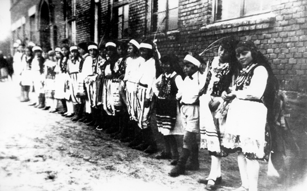 Rok i miejsce wykonania: 12.05.1935 r., Irządze, gm. Irządze, pow. zawierciański, woj. śląskie.

Fotografia przedstawia grupę dzieci w różnym wieku, ubranych w stroje ludowe (z elementami stroju krakowskiego). Stoją one w szeregu wzdłuż ściany murowanego budynku. Według nadawczyni zdjęcia zostało ono zrobione w czasie gminnego święta przysposobienia wojskowego i wychowania fizycznego w Irządzach.

Na odwrocie zdjęcia napis: „Grupa krakowska na święcie gm. wych. fiz. i przysp. wojsk.. w Irządzach” (pisownia oryginalna).

Autor zdjęcia: nieznany.

Zdjęcie ze zbiorów prywatnych, nadesłała: Maria Milejska-Czaja z miasta Zawadzkie, pow. strzelecki, woj. opolskie.

Nr kat. 160-15