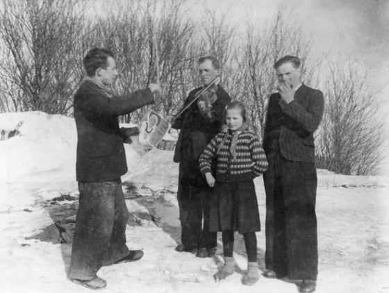 Rok i miejsce wykonania: zima, rok nieznany, Piaseczno, gm. Cegłów, pow. miński, woj. mazowieckie.

Fotografia przedstawia kapelę wiejską, składającą się z dyrygenta, dwóch mężczyzn grających na instrumentach muzycznych (jeden na skrzypcach, drugi na harmonijce ustnej), oraz dziewczynki, która trzyma się pod boki i śpiewa. Członkowie kapeli ubrani są dosyć lekko, zważywszy na zimowy krajobraz i sporą ilość śniegu wokół nich.

Autor zdjęcia: amator, nazwisko zapomniane.

Zdjęcie ze zbiorów prywatnych, nadesłał: Janusz Ciarkowski z Gdańska, pow. gdański, woj. pomorskie.

Nr kat. 141-7