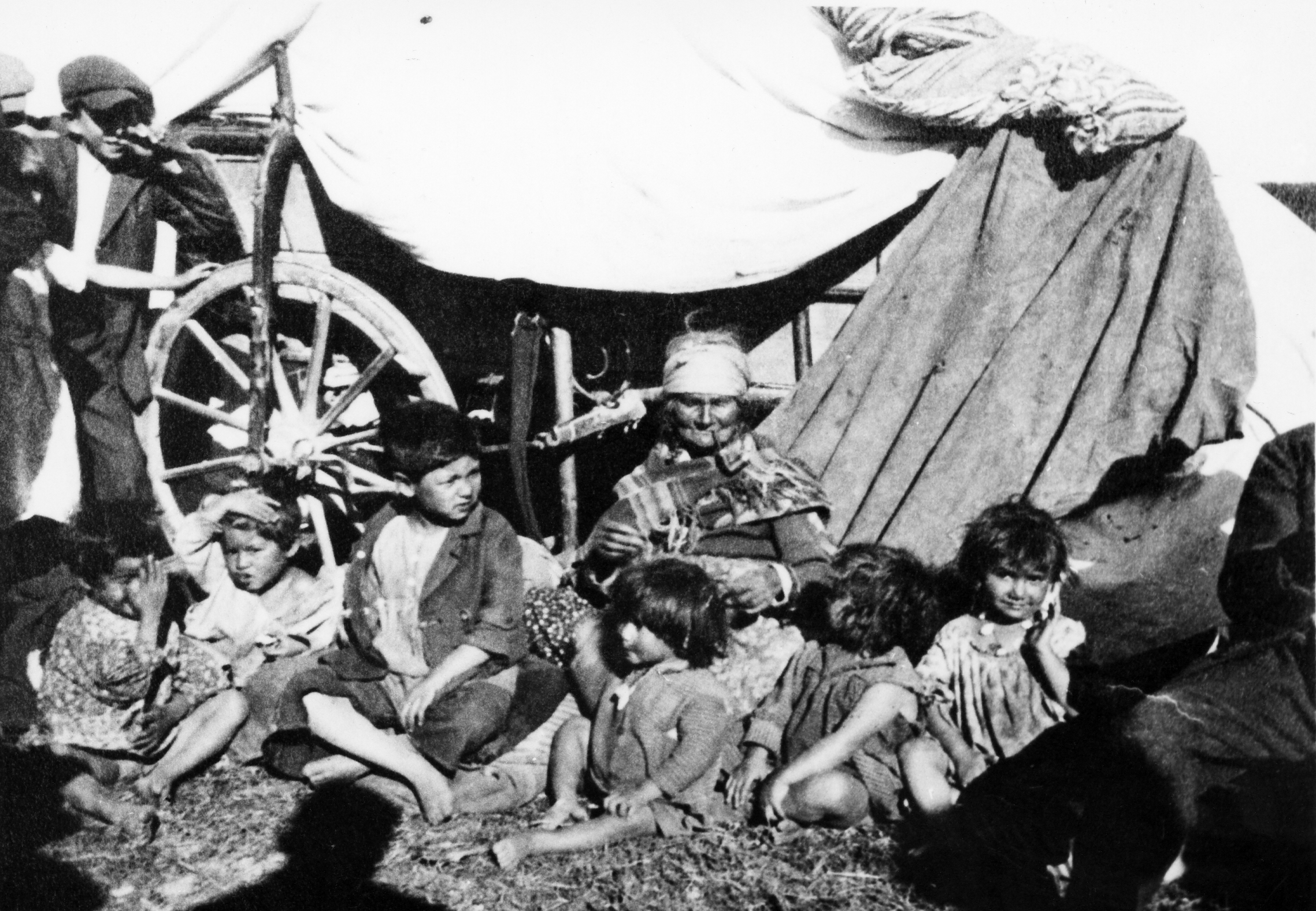 Rok i miejsce wykonania: lato 1936 r., okolice Łowicza, pow. łowicki, woj. łódzkie.

Fotografia przedstawia starszą kobietę palącą fajkę, w otoczeniu sześciorga ciemnych, bosonogich i umorusanych dzieci, które siedzą na trawie przed wozem cygańskim. Na wozie wietrzą się kołdry i koce. Za nimi, po lewej stronie, widać dwoje dzieci wiejskich przypatrujących się egzotycznej gromadce: fragment postaci dziewczęcej oraz chłopca opartego o koło wozu.

Na odwrocie zdjęcia opis: „Rodzina cygańska. Wykonane przez mojego ojca Ryszarda. Okolice Łowicza. W tych okolicach biwakowało kilka rodzin cygańskich”. 

Autor zdjęcia: Ryszard Bratkowski, ojciec nadawcy.

Zdjęcie ze zbiorów prywatnych, nadesłał: Jerzy Bratkowski z Łodzi, woj. łódzkie.

Nr kat. 307-3