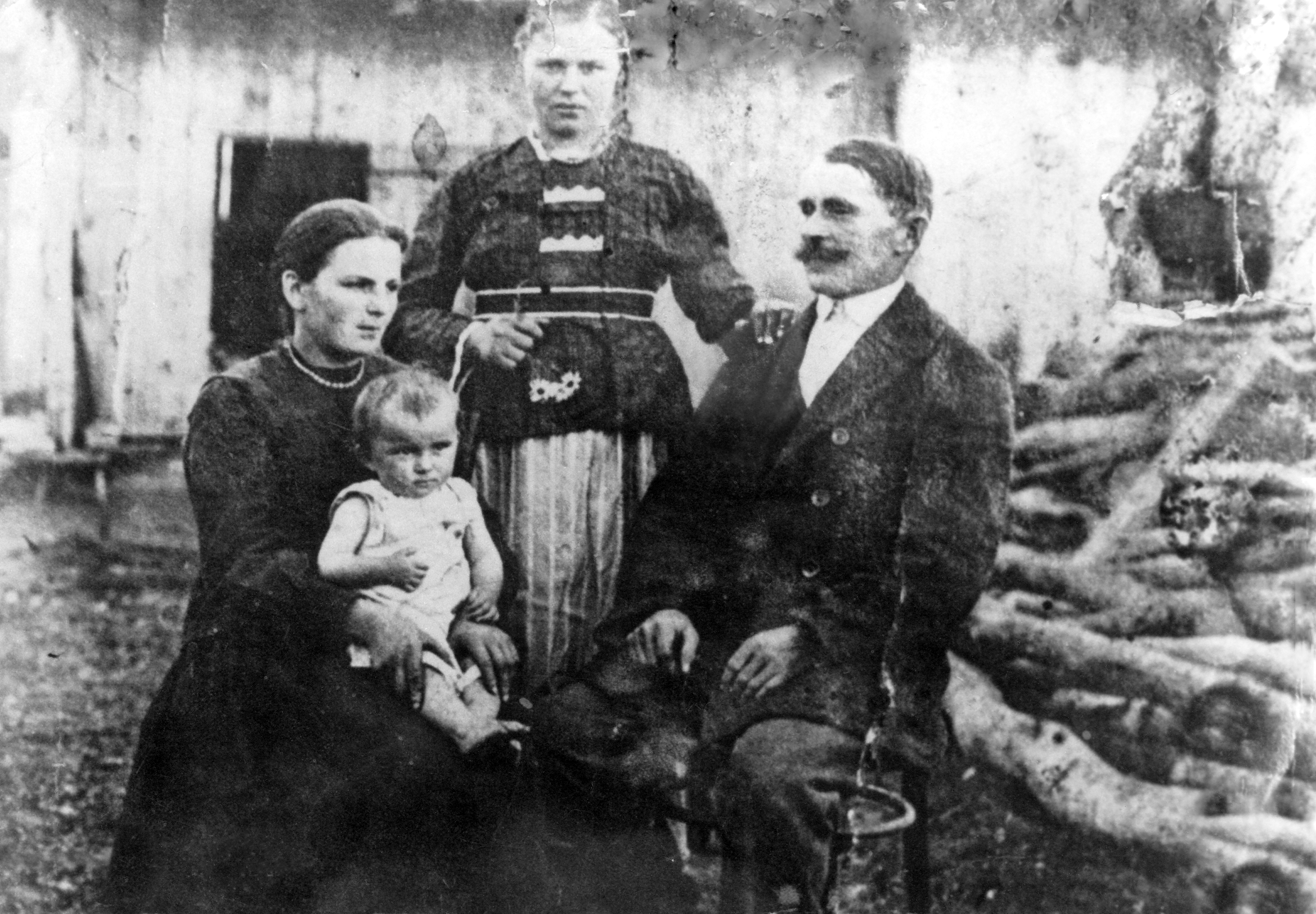 Rok i miejsce wykonania: 1925 r., wieś w powiecie i gminie Żydaczów, przed II wojną światową woj. stanisławowskie, obecnie Ukraina.

Fotografia przedstawia cztery osoby siedzące przed widocznym w tle ubogim domostwem. Po prawej stronie siedzi mężczyzna z ciemnymi wąsami, a obok niego kobieta z gładko zaczesanymi włosami trzymająca na kolanach niemowlę. Za nimi stoi kilkunastoletnia jasnowłosa dziewczyna o masywnej budowie ciała, trzymająca lewą dłoń na ramieniu mężczyzny. Mężczyzna ubrany jest w białą koszulę i ciemny, dwurzędowy, krótki płaszcz, zaś kobieta w długą czarną sukienkę, a na szyi ma drobne korale. Dziecko ma na sobie jasny kaftanik bez rękawów, a dziewczyna bluzkę z paskiem i jasną, długą, plisowaną spódnicę. Stroje pozującej do zdjęcia rodziny dokumentują regionalny ubiór i styl epoki.

Z relacji nadawcy zdjęcia wynika, że przedstawia ono jego rodzinę ze strony nieżyjącej już babci. Pierwsza z lewej to siostra babci, Magdalena, wraz z córką Anielą. Po prawej stronie siedzi jej mąż Michał Greń, a między nimi babcia nadawcy, Wiktoria Janik, później Majdak, która podczas wykonywania zdjęcia była jeszcze panną.

Autor zdjęcia: nieznany. Zdjęcie ze zbiorów prywatnych, nadesłał: Krzysztof Rakoczy z Bielsko-Białej, pow. bialski, woj. śląskie.

Nr kat. 264-1