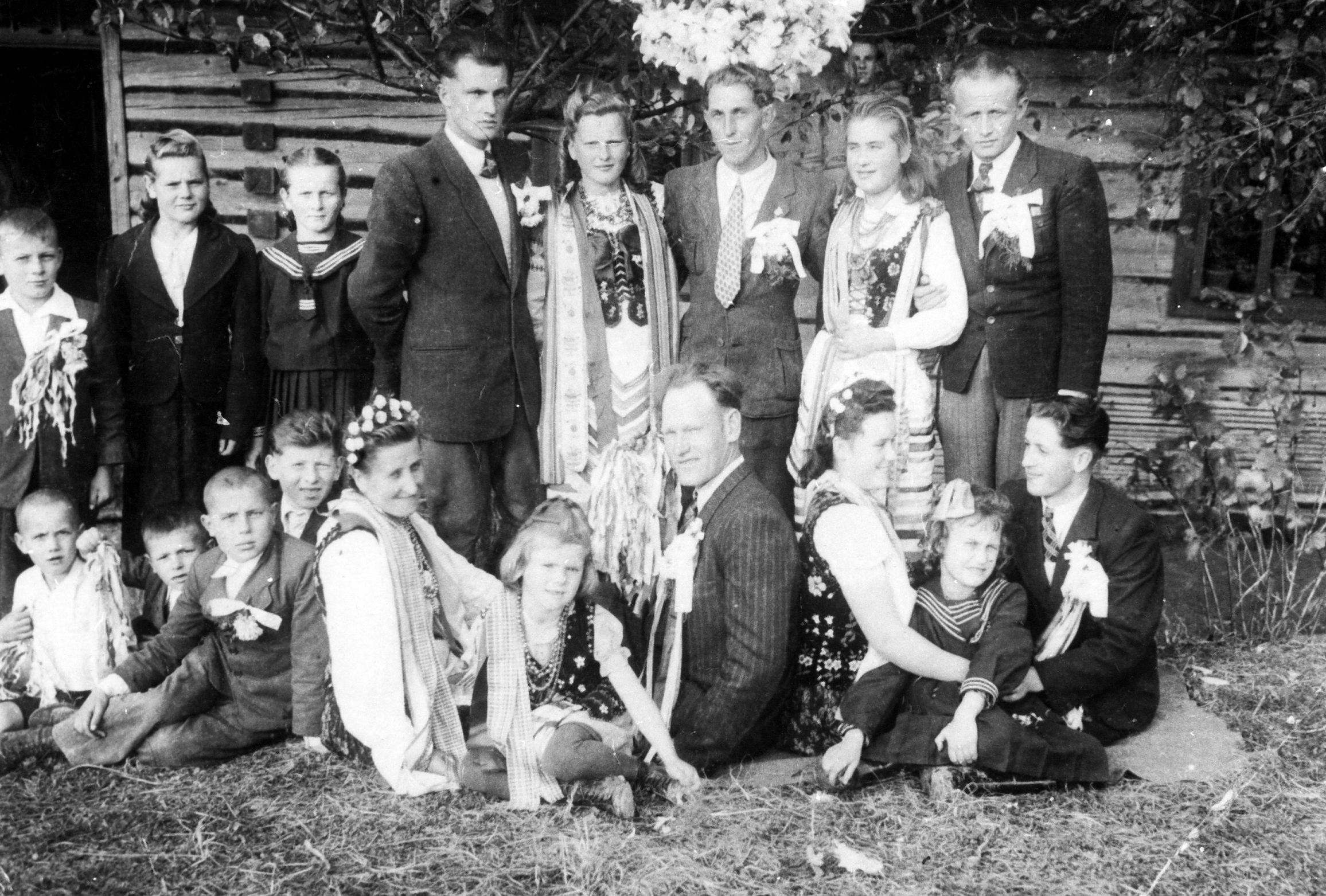 Rok i miejsce wykonania: 1948 lub 1949 r., Handzlówka, gm. Łańcut, pow. łańcucki, woj. podkarpackie.

Fotografia przedstawia grupę gości weselnych w różnym wieku. Uwagę zwracają cztery kobiety w strojach regionalnych (typu krakowskiego) oraz pięciu mężczyzn w garniturach, białych koszulach, krawatach. W butonierkach mają małe bukiety przybrane wstążkami. Są to osoby około dwudziestokilkuletnie. Towarzyszy im grupa dzieci w wieku od około trzech do kilkunastu lat. Za wyjątkiem jednej dziewczynki, która jest w stroju regionalnym, wszystkie pozostałe ubrane są w odświętne, zwykłe stroje. Wszyscy chłopcy, podobnie jak młodzi mężczyźni, mają przypięte bukiety.

Według właścicielki zdjęcia fotografia przedstawia gości weselnych: swatów (drużbów) i „starsze” oraz „młodsze” drużki (druhny) w strojach ludowych.

Autor zdjęcia: nieznany.

Zdjęcie ze zbiorów prywatnych, nadesłała: Maria Magryś z Rzeszowa, woj. podkarpackie.

Nr kat. 336-13